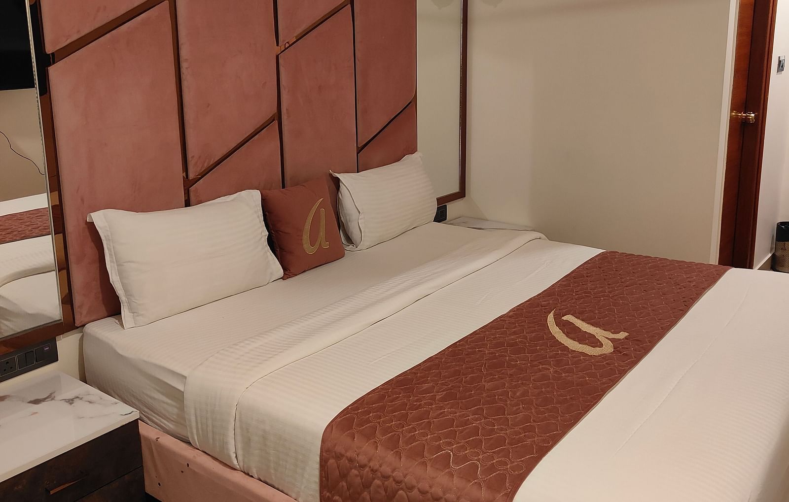 side view of a double bed with two pillows with a cushion kept over it at the compact room - Astra Hotels and Suites, Koramangala