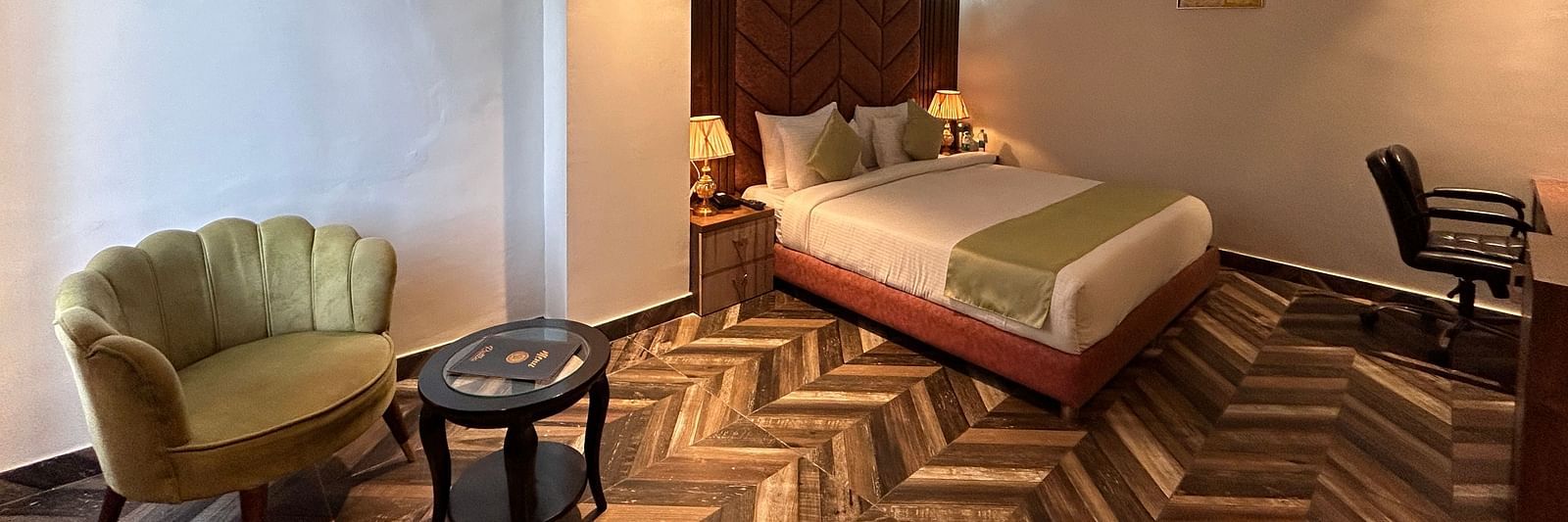 Image of Super Deluxe Room at DLS Grand Luxotica, Dehradun featuring a sitting space including a couch and a coffee table placed at a distance from the plush bed under warm lighting