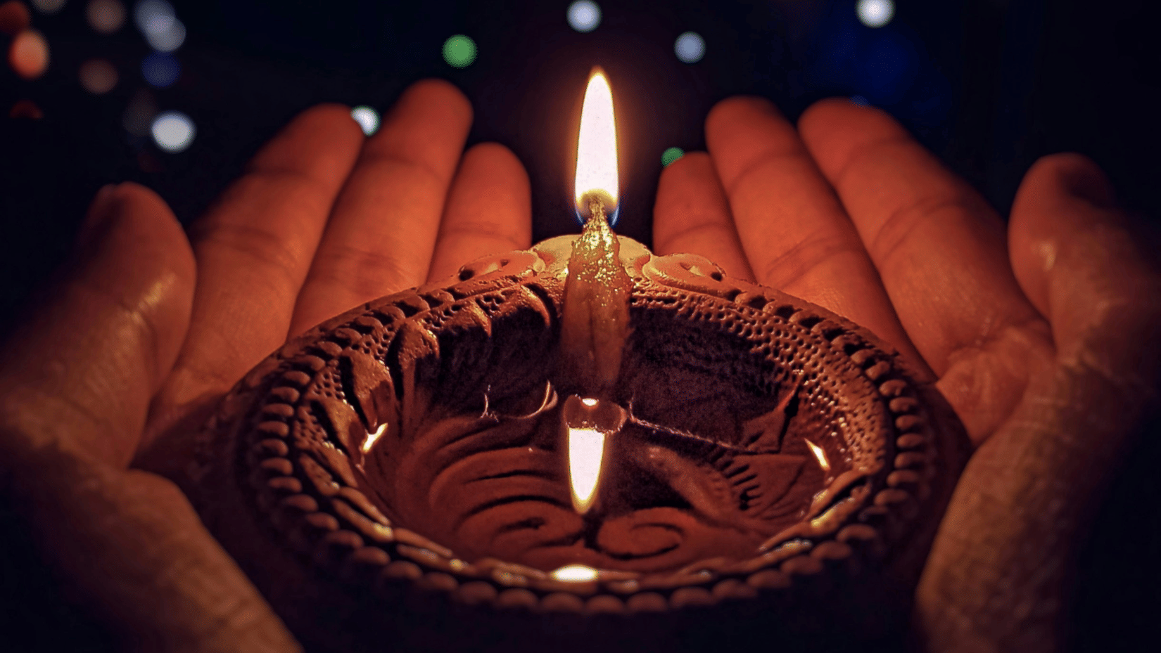 Hand holding a traditional clay lamp with colourful lights glowing softly in the background during Diwali in Chennai