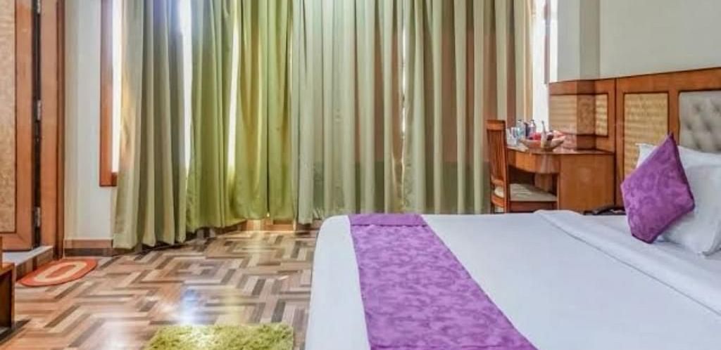 A spacious bedroom with rich wooden flooring, green drapes, and a purple-accented bed for a cosy stay - Pemaling Lords Eco Inn Guwahati