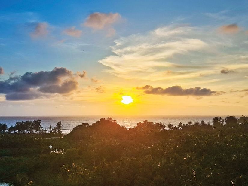 The sunrise view over the trees and beach, set against a slightly cloudy sky, offers a serene scene at Cloud9 Sarovar Premiere, Palolem Goa