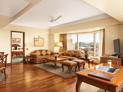 A spacious suite living area at Ramada Plaza by Wyndham Palm Grove, featuring elegant wooden flooring, plush seating, and large windows with city views.