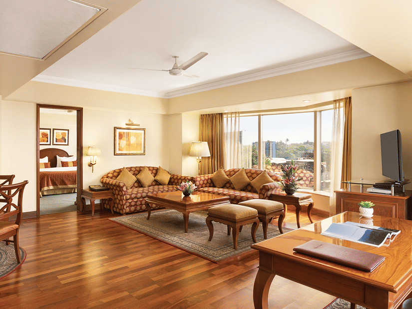 A spacious suite living area at Ramada Plaza by Wyndham Palm Grove, featuring elegant wooden flooring, plush seating, and large windows with city views.