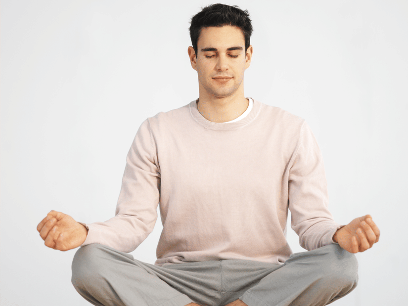 Man sitting cross-legged and meditating with eyes closed, practicing mindfulness in a calm, minimalist setting.