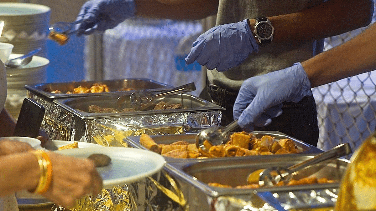 People serving food from chafing dishes onto plates at a buffet table.