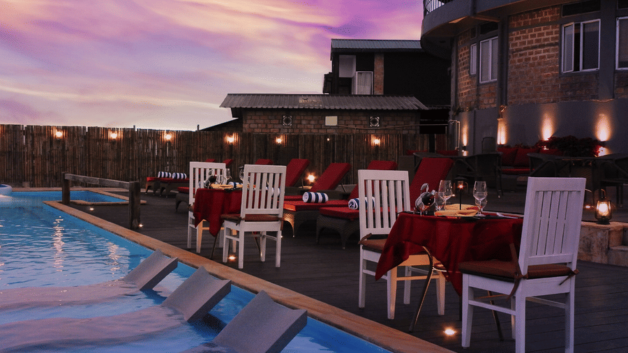 Poolside dining setup with white chairs and red-draped tables beside the swimming pool under a pink sunset sky at Polo Resort Cherrapunji.