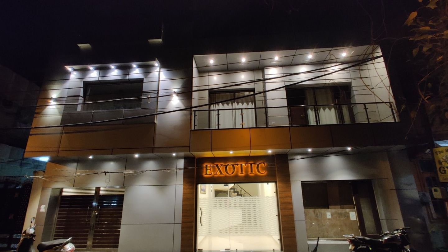 An exterior shot of Hotel Exotic Amritsar at night, showing the illuminated signage and the modern facade of the building.