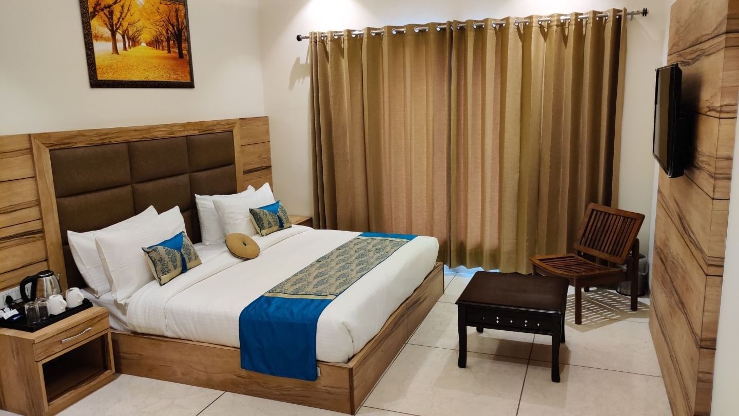 A hotel room at Hotel Exotic Amritsar with a king size bed, a padded headboard, and a white duvet with a blue and gold patterned throw blanket. 