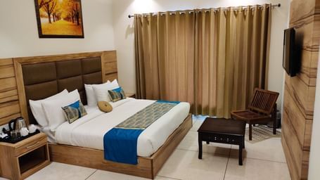 A hotel room at Hotel Exotic Amritsar with a king size bed, a padded headboard, and a white duvet with a blue and gold patterned throw blanket. 