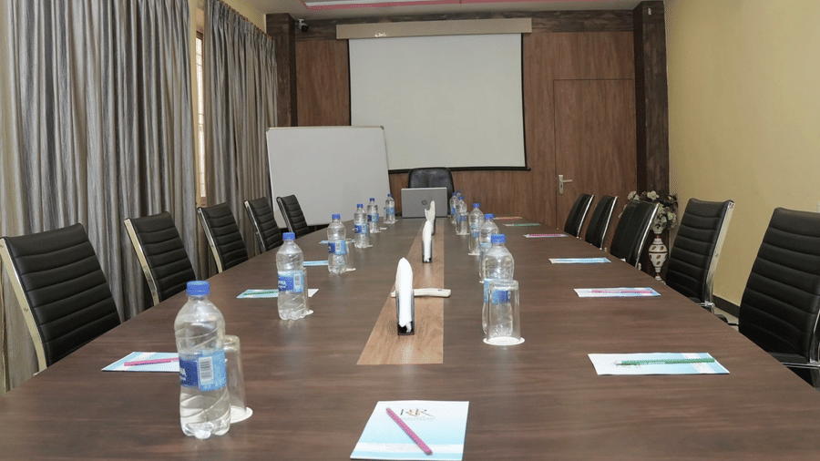 A spacious meeting room featuring a large wooden table and a white presentation board at the Ram Bhawan Ram Yamuna Prasad Hotel and Resort.