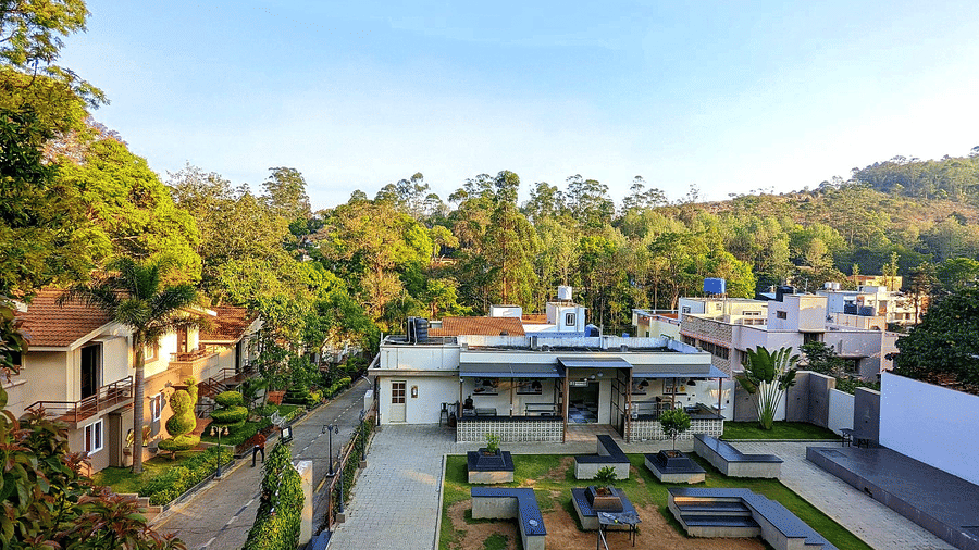 TGI Star Holidays Resort courtyard with benches and tables, surrounded by houses, greenery, and hills under clear sky.