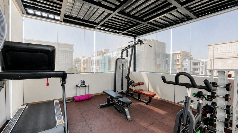 Rooftop fitness area at Hotel Kyzen Smart Stays Madhapur with multiple gym equipment including a treadmill, cycling machine, and weight training stations with glass walls.
