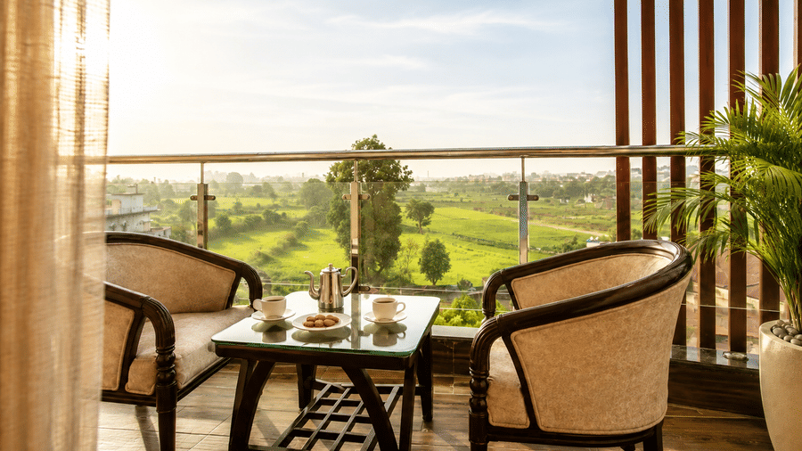 Balcony seating area with a table and chairs overlooking green gardens at Eastlynn Resort, Rishikesh.