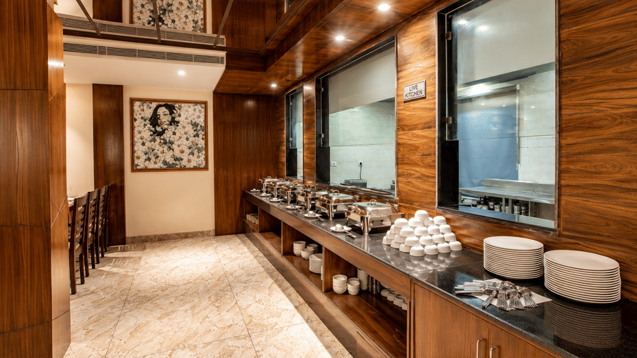 Buffet counter along a corridor with dark wood cabinetry and covered dishes at Eastlynn Resort, Rishikesh.