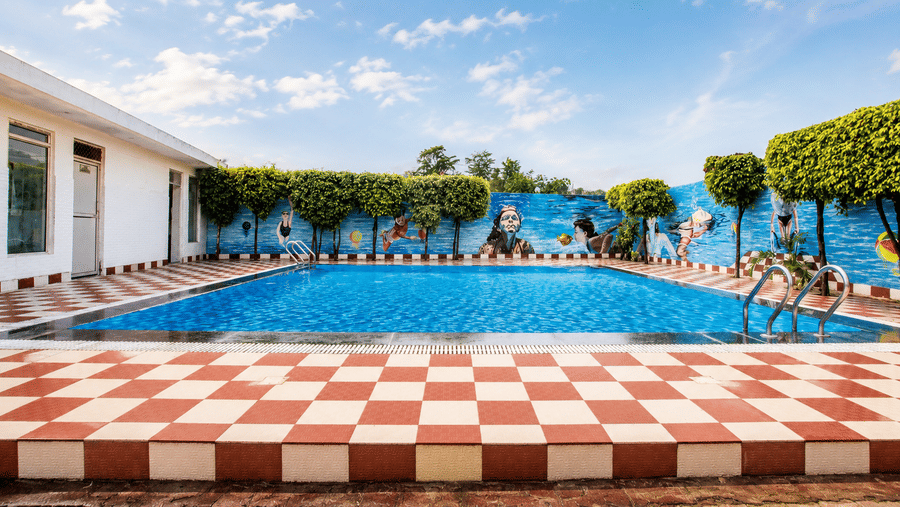 Outdoor swimming pool with a red and white checkered deck surrounded by greenery at Eastlynn Resort, Rishikesh.