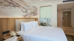 Premium Double Bed Room at Riviera Sarovar Portico, Pathankot, featuring a king size bed, wall-mounted television, wooden flooring, work desk, wardrobe, and an ensuite bathroom.