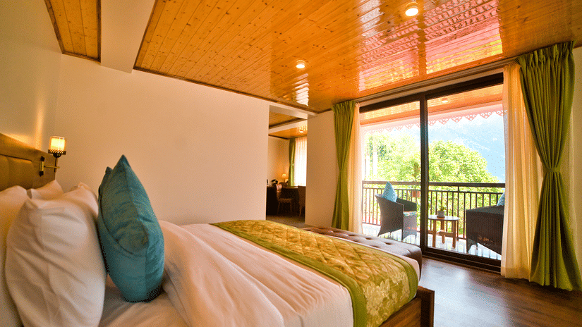 Spacious bedroom at Voyage Songfum Retreat with a plush bed, soft teal cushions, wooden ceiling, and a scenic private balcony overlooking the hills.