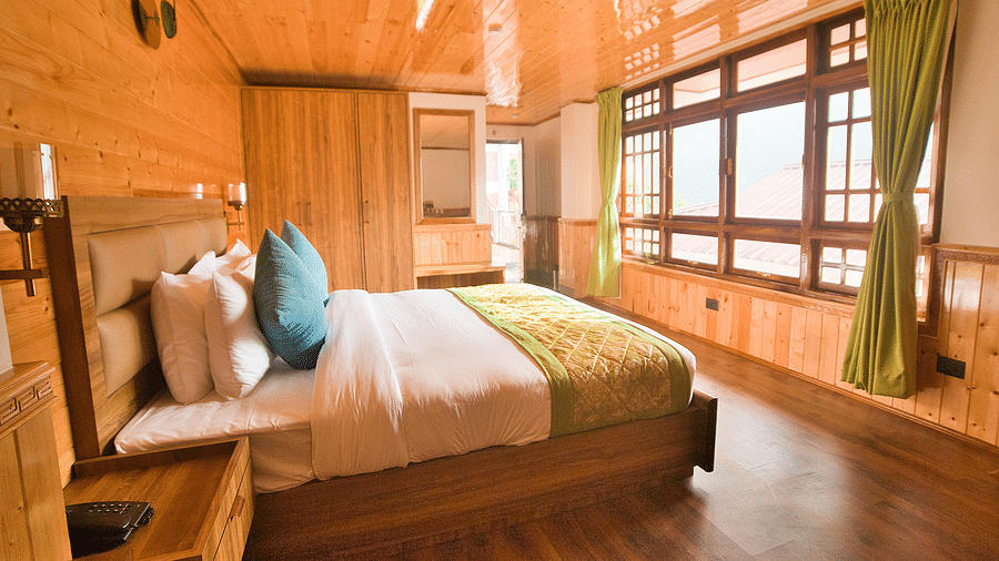 A room featuring a double size bed, a window covered with curtains, and a bedside table at the Voyage Songfum Retreat, Gangtok.