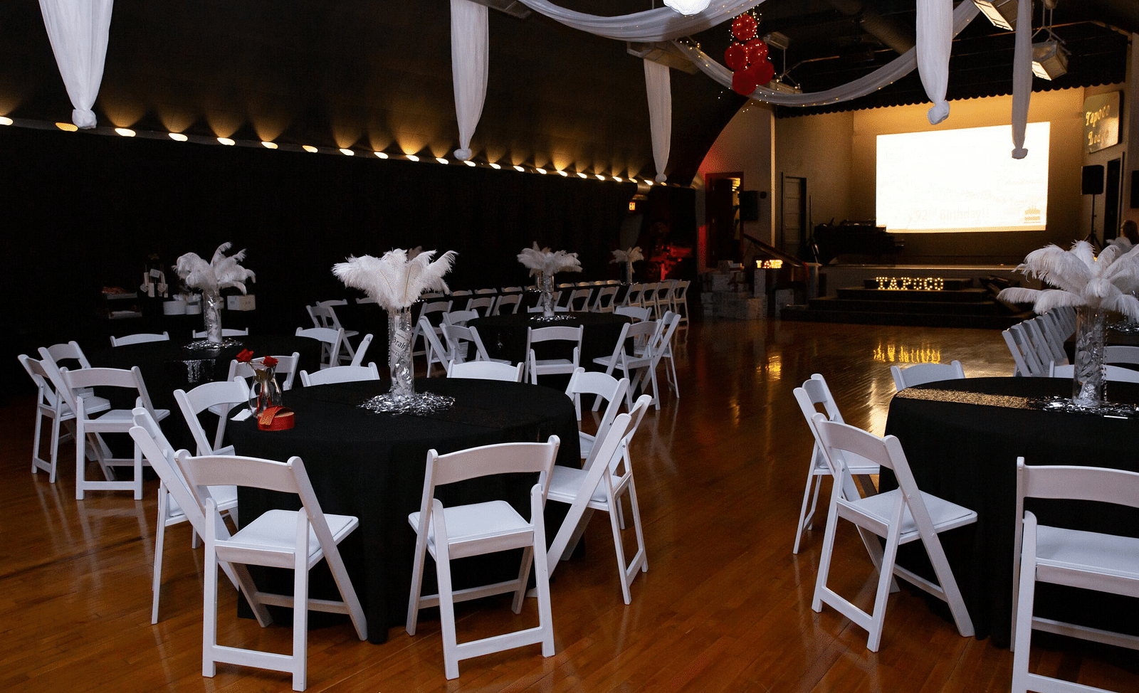 full view image of the Tin Can Theater featuring the round tables and the folding chairs with a projector screen at the far end - Historic Tapoco Lodge