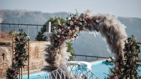 Floral and pampas grass arch decoration beside the poolside at Polo Resort Cherrapunji with a white bench and stone wall in background.