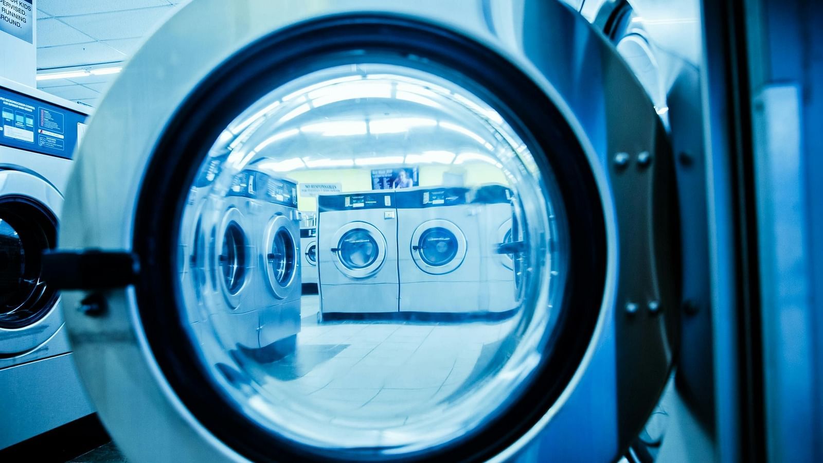The interior of a laundromat, focusing on a front-loading washing machine with its door open, revealing other washing machines in the background.