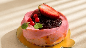 A small, pink, fruit-topped tart sits on a light-colored surface with strong shadows, with two whole strawberries visible in the background at Gemini Continental 
