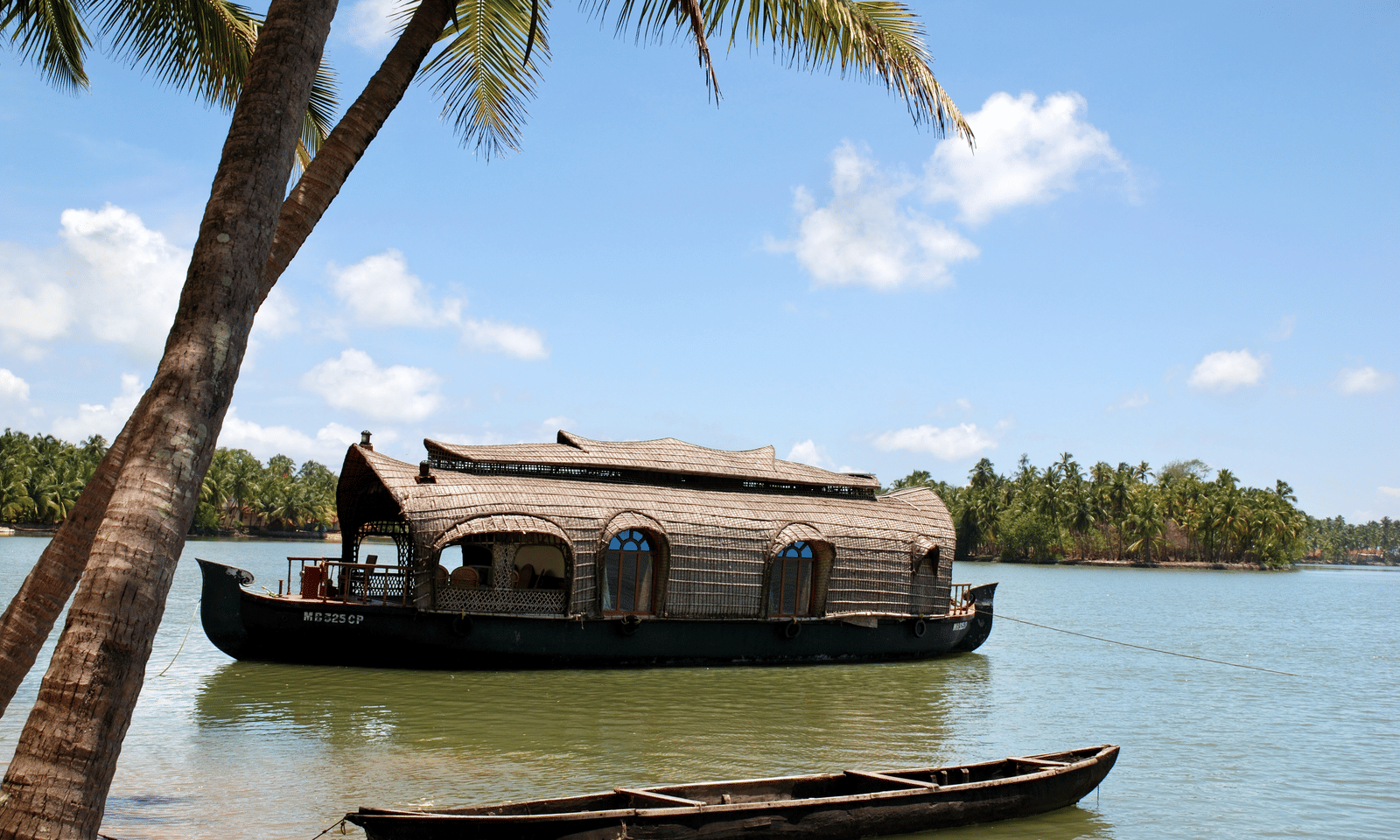 Docked houseboat with a curved roof on calm backwaters, with trees and sky in the background at Paradise Lagoon Resort.