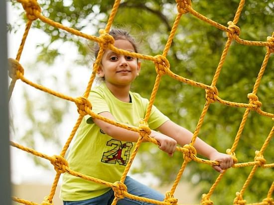 Kid on a commando net ride at inflated trampoline surrounded by trees at Themis Mudhouse - A Nature's Retreat Resort & Wellness
