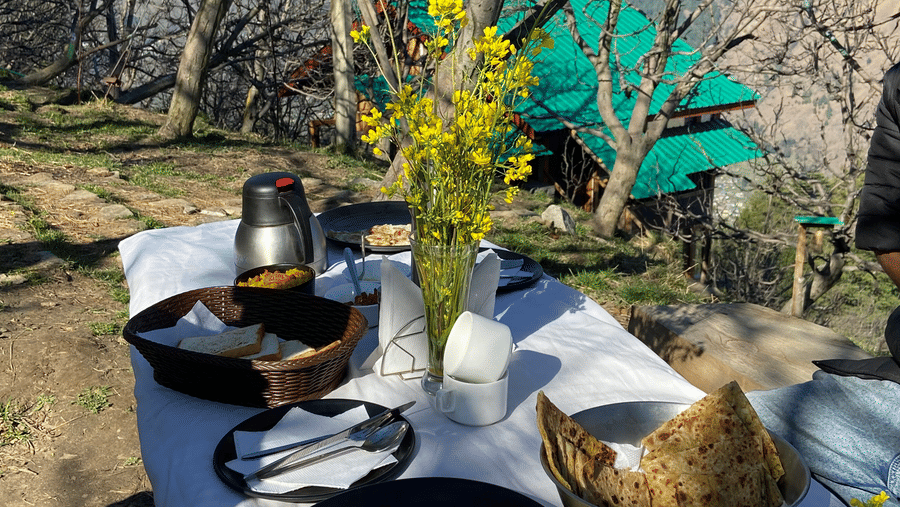 A neatly-arranged tabled with breakfast along with fresh flowers kept in a vase in the middle overlooking the beautiful Himalayas at Amara Upepo -The Sky Village, Manali.