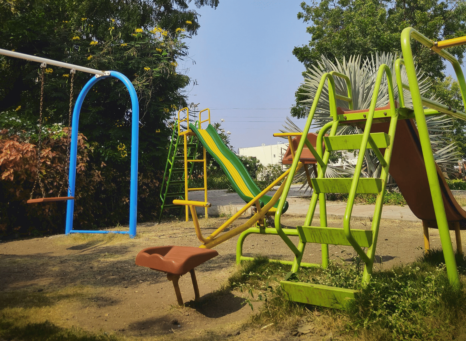 An outdoor children's playground featuring a metal climbing frame with a slide and structures, surrounded by trees under a clear sky.