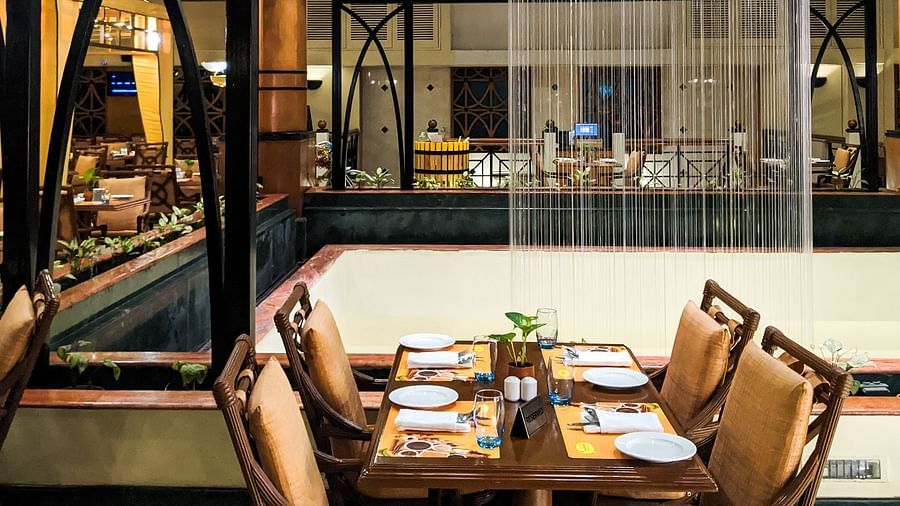 Elegant dining setup in a restaurant with wooden tables and chairs, viewed through a glass pane with vertical blinds, showcasing an inviting atmosphere.