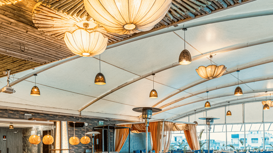 Stylish interior of The Papaya Tree Hotel’s Nazara restaurant showcasing golden ceiling decor, artistic chandeliers, and neatly arranged dining tables in a contemporary setting.