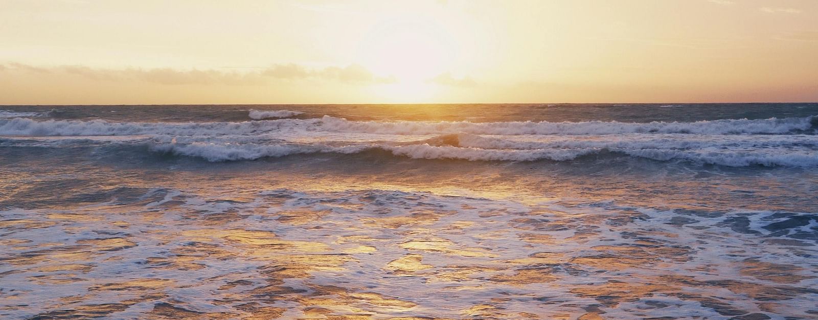 A serene ocean scene at sunset with soft waves breaking on the shore and a glowing sky in the background.