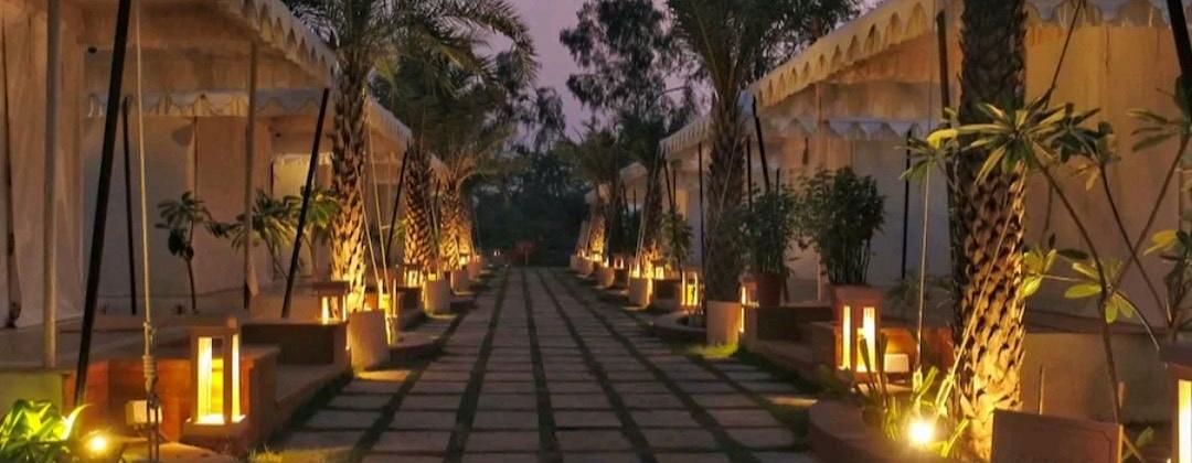 A stone pathway leads through Ananta Spa and Resort, Pushkar, offering a Pushkar tent stay experience, lined with canvas tents, illuminated by warm lights at twilight.