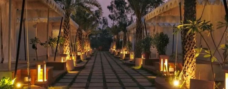 A stone pathway leads through Ananta Spa and Resort, Pushkar, offering a Pushkar tent stay experience, lined with canvas tents, illuminated by warm lights at twilight.