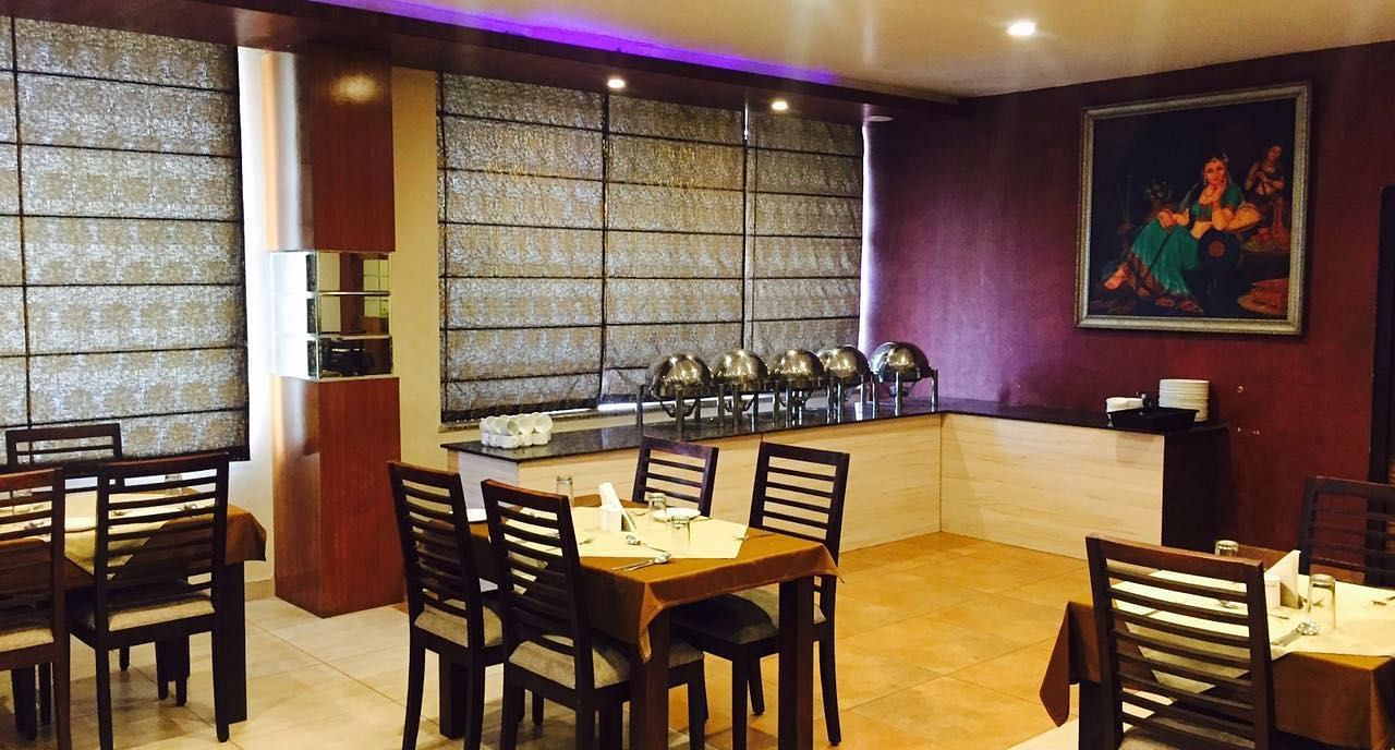 A dining room with a serene ambience, featuring a mix of wooden chairs and tables and a decorative screen - TGI Apple Inn, Jaipur 