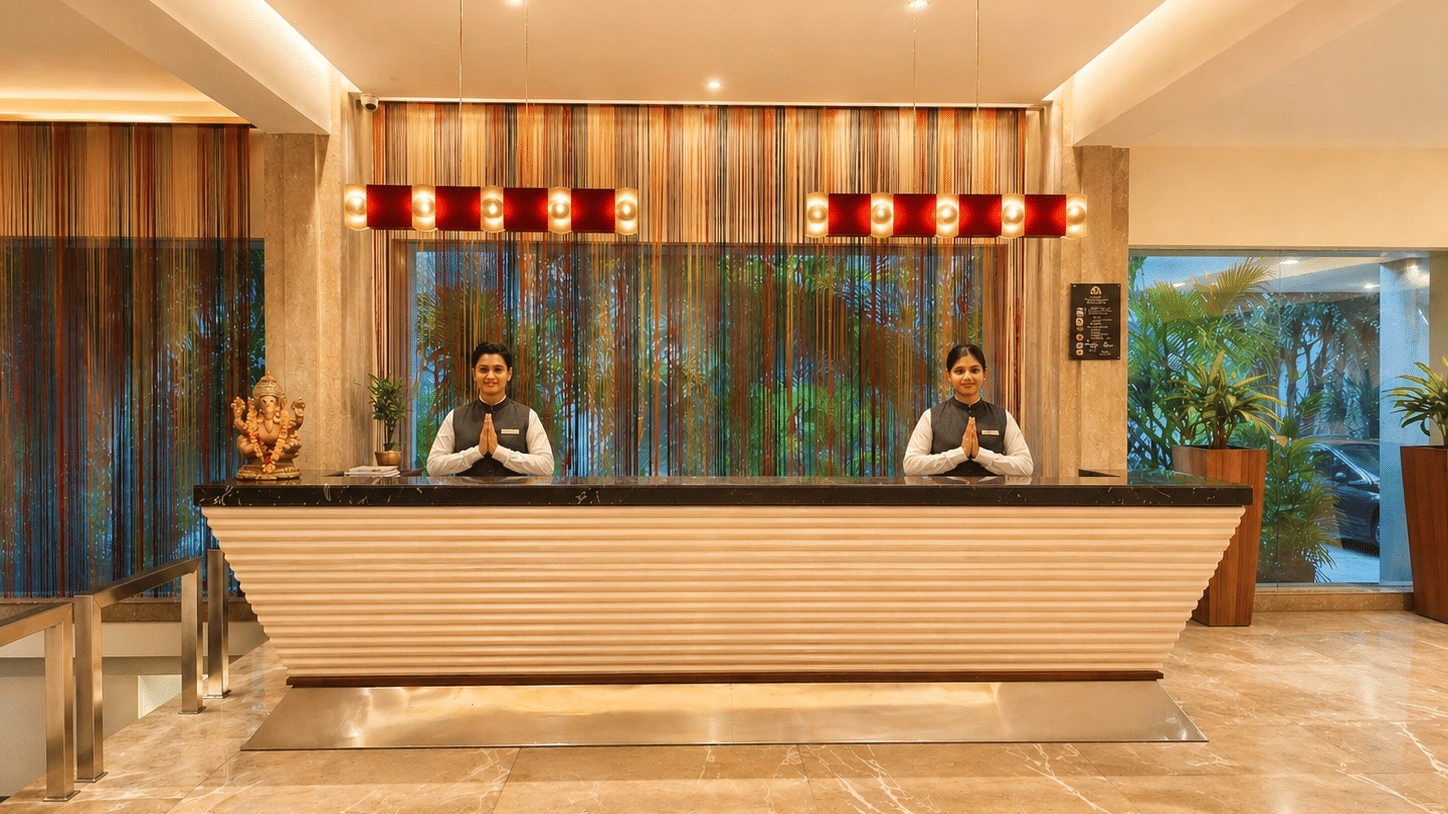 Reception entrance at Pride Premier Pune with people posing namaste, plants, and an elongated desk.
