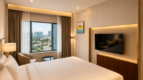 A Premium Room at Pride Plaza Indore showing a double bed, a wall-mounted television on a panel, and a window with curtains overlooking a city view.