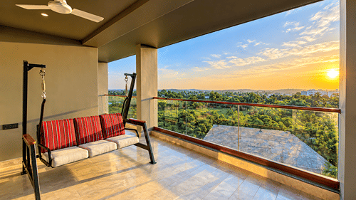 Spacious private balcony with a comfortable swing chair offering panoramic sunset and greenery views at Sarovar Portico Gir Executive Suite.