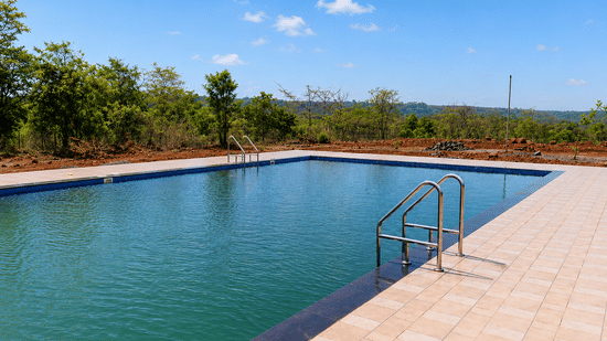 Swimming pool at Nature Trails Kundlaika featuring a steel entry ladder, granite edge, and natural forest backdrop.
