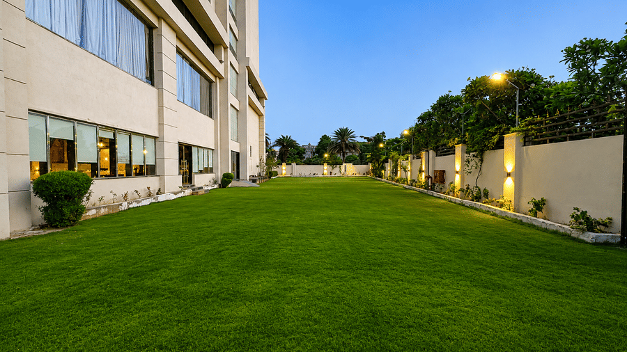 Spacious hotel lobby at Golden Tulip Kukas Jaipur with marble floors, dining setup on the left, indoor plants, and large windows allowing natural light.