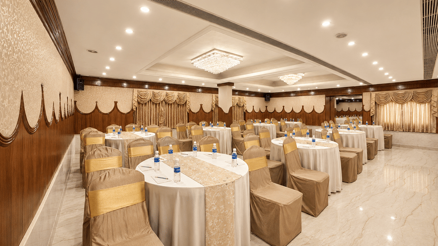 A hall with multiple chairs, chandeliers, and a stage at Raj Park, Chennai.