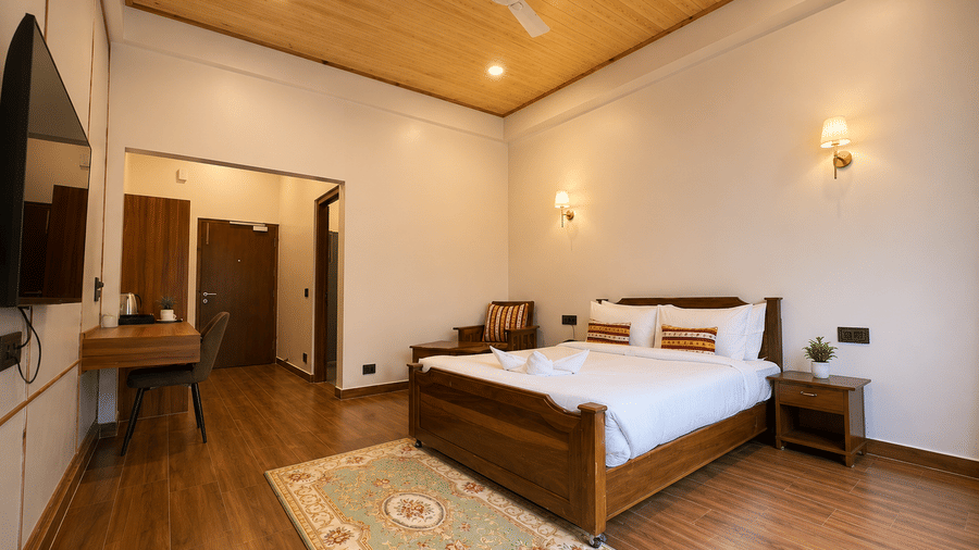 Wooden double bed, patterned rug, wall lamps, and work desk setup in a spacious room at Summit Rungkhung Village Resort.