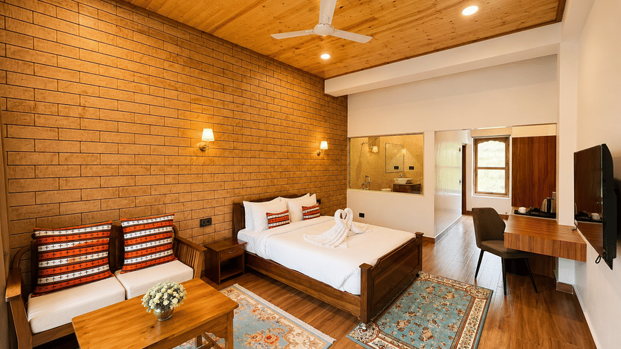 Bedroom with wooden double bed, seating area, work desk, brick wall, and ceiling fan at Summit Runghkhung Village Resort.