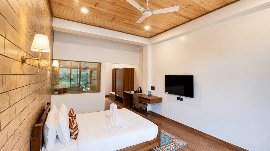 Double bed with white linens, wall-mounted TV, work desk, and wooden ceiling at Summit Rungkhung Village Resort.