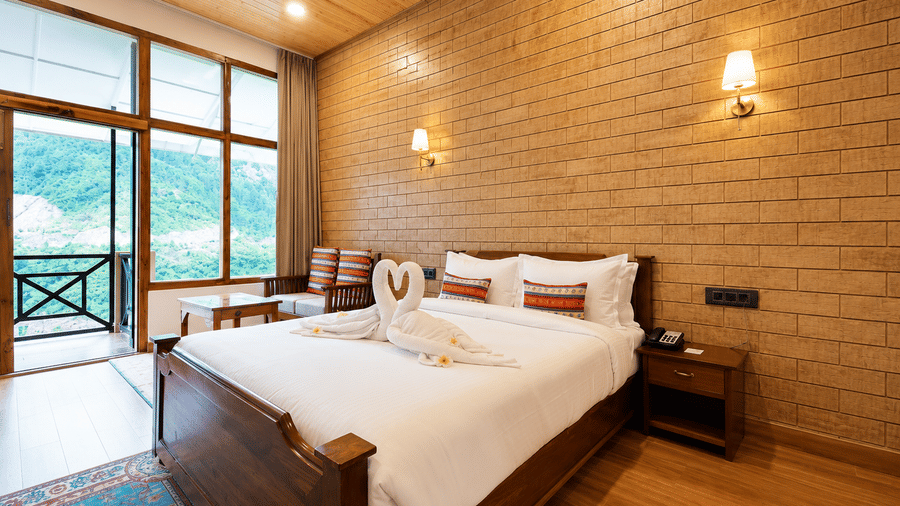 Double bed with bedside table, wall lamps, and large glass doors leading to a balcony at Summit Rungkhung Village Resort.