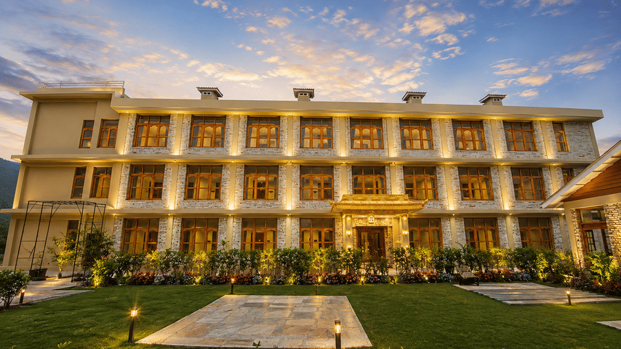 Exterior view of Summit Rungkhung Village Resort - The Signature Collection showcasing a multi-storey illuminated building, lush green lawn, and sunset sky.