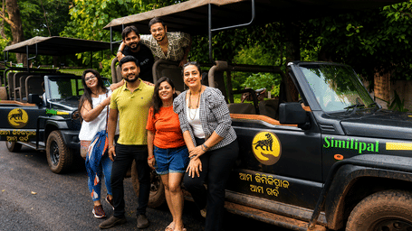 Group of travellers posing beside an open safari jeep on a forest trail, enjoying an outdoor wildlife and nature adventure