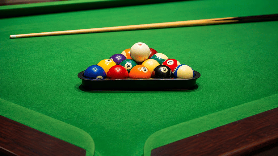 A close up view of a snooker table at Hotel Sonar Bangla, Mayapur, featuring a rack of billiard balls, a cue stick, and pocket corners.