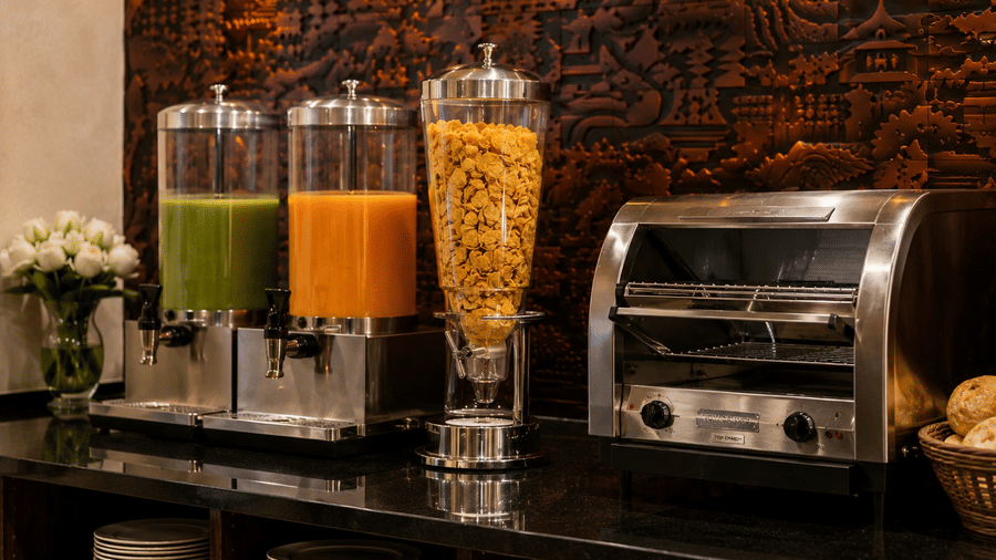 Beverage station at Lime Tree Hotel & Banquet, Jaipur, featuring juice dispensers filled with green and orange juices next to a toaster.